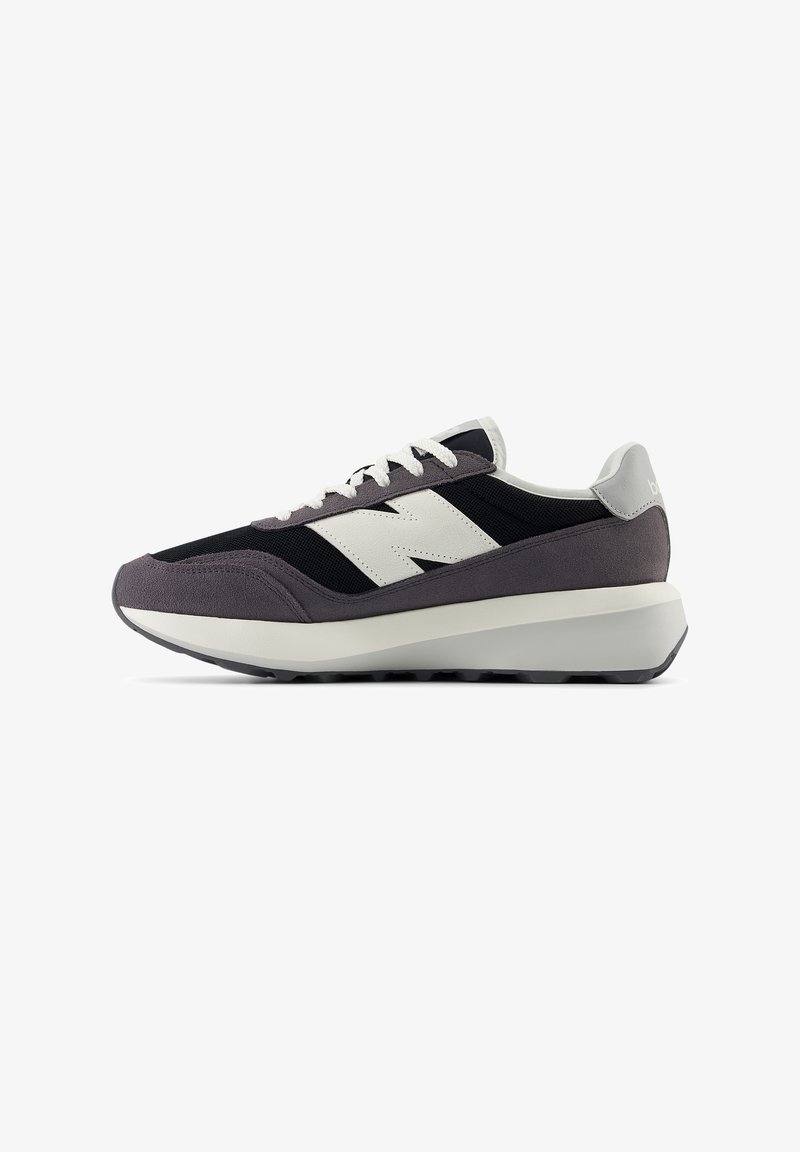 Baskets noires et grises avec logo blanc et lacets blancs, semelle épaisse blanche et grise, vues de côté sur fond blanc.