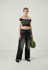 Μπούστο με ασπρόμαυρες ριγέ λωρίδες και ανοικτούς ώμους, μαύρο τζιν με ψηλή μέση και αντίθετη ραφή, συνοδευόμενο από πράσινη καπιτονέ τσάντα.