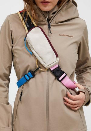 Heuptas met beige en kastanjebruine stof, verstelbare roze en blauwe banden, ronde gouden ringaccent, gedragen op een tan-kleurige jas.