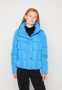 Doudoune bleue avec un col haut, fermeture à pression et texture matelassée. Caractéristiques : poches latérales et finition brillante.