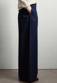 Pantalon large bleu marine avec une taille haute élastique et des poches latérales, fabriqué à partir d'un tissu lisse et léger.