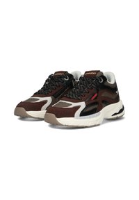 Zapatillas marrones y negras que cuentan con materiales de malla y ante, superposiciones texturizadas y una suela blanca con una ligera curvatura. Incluyen acentos reflectantes.