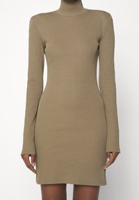 Ribbede, langærmede kjole i khaki med høj hals. Tætsiddende pasform, glat tekstur, knælang med diskret syning langs kanten.
