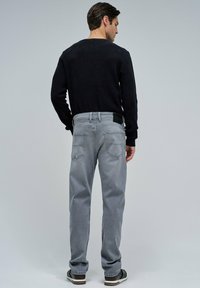 Jeans de denim gris con un corte recto y bolsillos en la parte trasera, combinados con una blusa negra de manga larga. La tela tiene una textura suave.