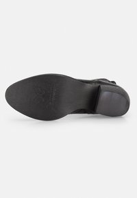Suela de zapato negra con una textura suave y mate y una ligera curvatura. Presenta una marca grabada en el material y un diseño de punta redondeada.