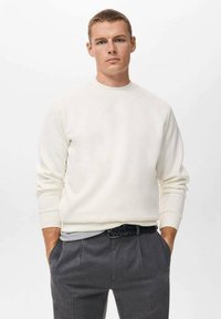 Sudadera de crema clara con cuello redondo, mangas largas y puños acanalados. Combinada con pantalones grises y un cinturón negro texturizado.