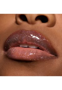 Glansig naken läpp med skimrande, iriserande glitter. Slät textur, något fyllig form som framhäver en naturlig läppkontur.