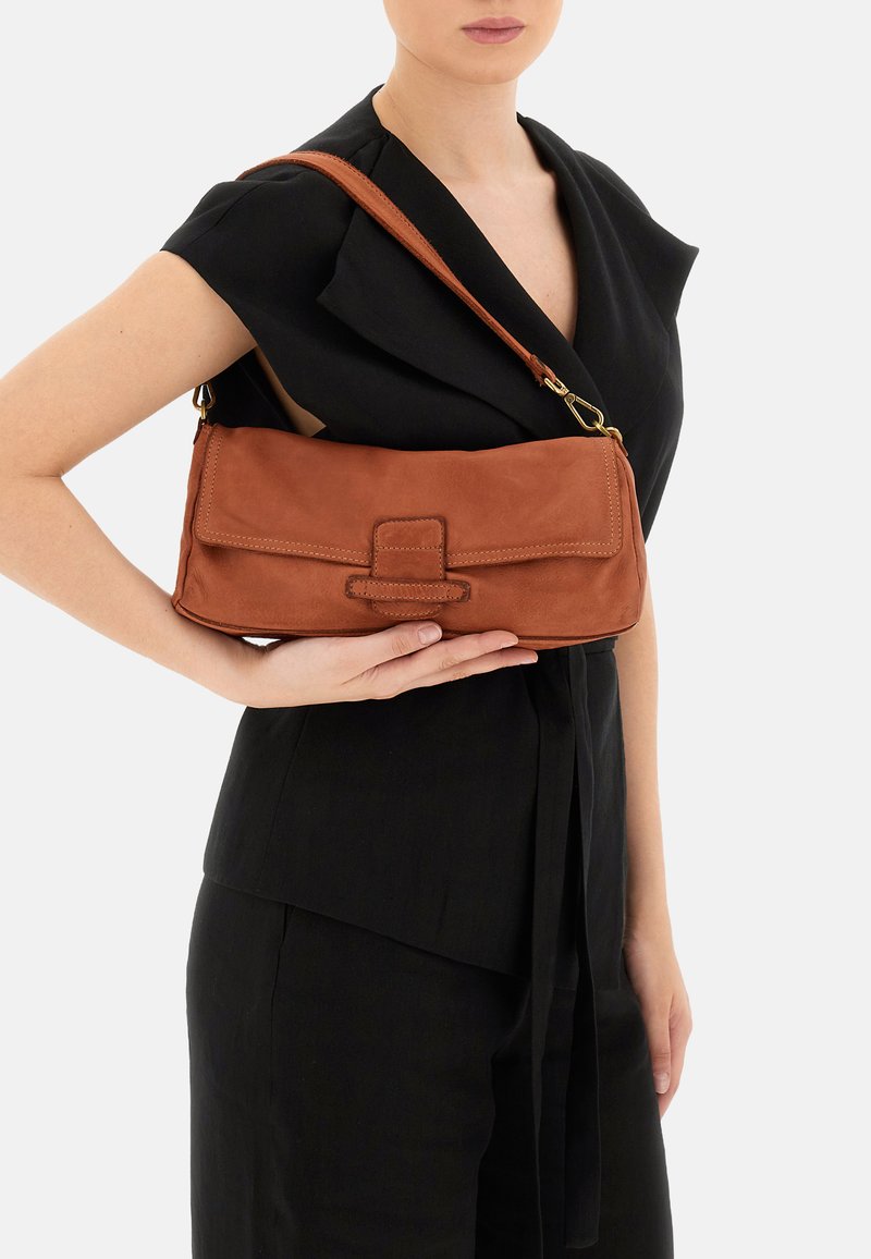 Borsa a spalla in pelle marrone con forma piatta, dotata di una patta pieghevole e di una tracolla, tenuta in mano su uno sfondo neutro.