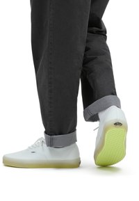 Witte sneakers met een doorzichtige groene zool, leren bovenwerk, vetersluiting en Vans-logo op de hiel, gecombineerd met grijze, opgerolde broeken.