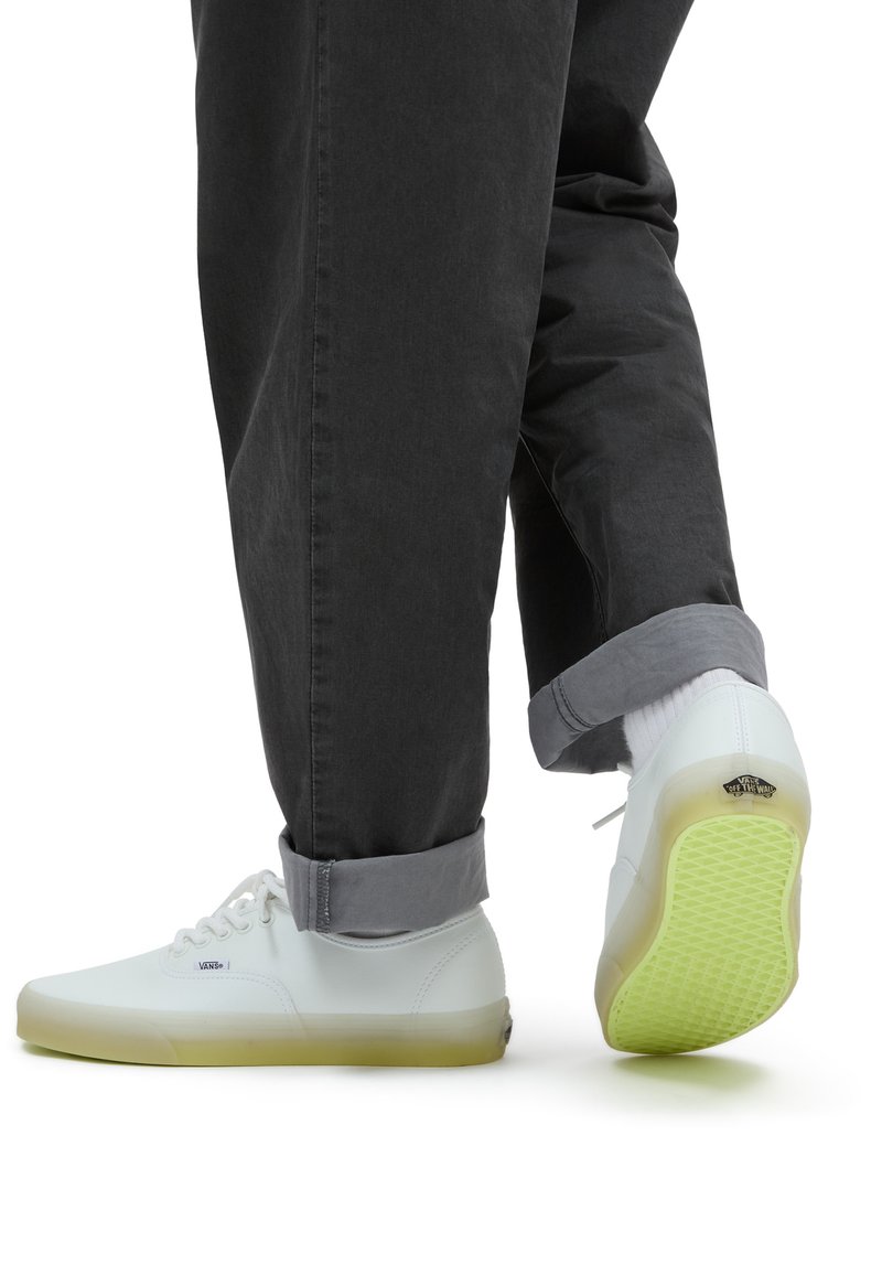 Witte sneakers met een doorzichtige groene zool, leren bovenwerk, vetersluiting en Vans-logo op de hiel, gecombineerd met grijze, opgerolde broeken.