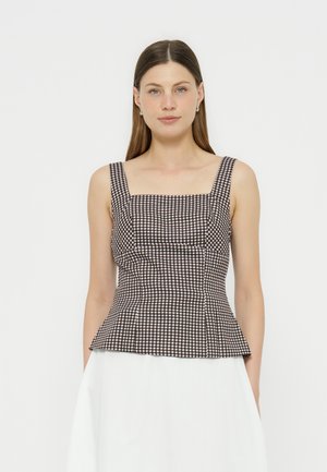Mujer que lleva una blusa sin mangas de cuadros en blanco y negro con escote cuadrado y cintura ajustada, combinada con una falda blanca, sobre un fondo liso.