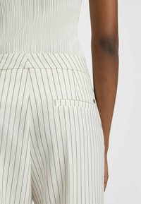 Witte gestreepte broek met een getailleerde pasvorm, voorzien van dunne strepen in donkergrijs, een achterzak en een gladde stoffen textuur.