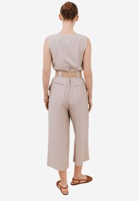 Beige urringtopp utan ärmar med texturerad tyg, parat med högmidjade, vida byxor och ett vävt bälte. Sandaler fulländar looken.