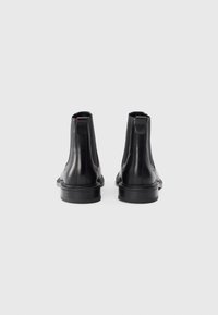 Black leather ankle boots with a smooth finish, elastic side panels, and a rubber sole. Features minimal stitching and a heel tab.