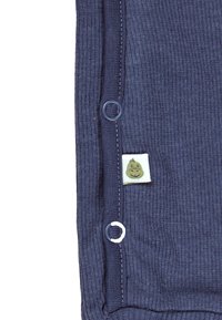 Marine-blau gerippter Stoff mit Knopf-Akzenten an der Seite, ausgestattet mit einem grünen und weißen Etikett, das ein lächelndes Charakterdesign zeigt.