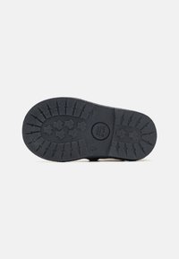 Suela de zapato de goma negra con patrones de dibujo y superficie texturizada. Presenta un logotipo circular y diseños en forma de estrella para mejorar el agarre.