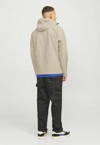 Beige waterproof jacket with a hood, paired with a blue shirt and black cargo pants featuring white stitching and practical pockets.