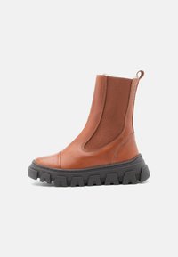 Brun läderankelboot med elastiska sidopaneler, svart klumpig sula, rund tå och bakre dragtab för enkel påtagning.