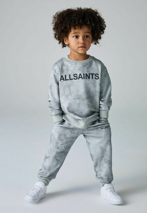 Grå bomulds sweatshirt og joggers med en blød tekstur, prydet med et sort "ALLSAINTS" logo, parret med hvide sneakers.