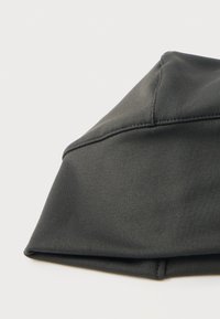 Μάσκα προσώπου από σκουρόχρωμο γκρι ύφασμα με ορατές ραφές, που βρίσκεται επίπεδη πάνω σε λευκή επιφάνεια.