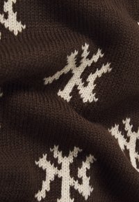 Brun strikket stoff med et teksturert mønster av hvite geometriske former og aksenter, som skaper en kontrast mot bakgrunnsfargen.