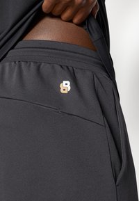 Μαύρο αθλητικό σορτσάκι με υφή και ορατό λογότυπο σε χρυσό και λευκό στη μέση. Επισημαίνεται από μια κομψή σχεδίαση.