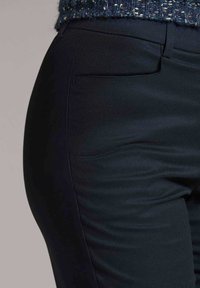 Dunkelblaue Hose aus glattem Stoff, mit schlankem Schnitt, diskretem Seitentasche und subtiler Textur ohne sichtbare Muster.