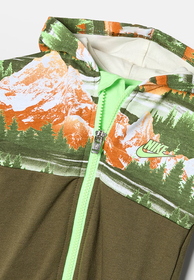 Veste zippée à capuche ornée d'un imprimé montagne et forêt en orange et vert, avec une fermeture éclair verte et le logo Nike sur la poitrine. Partie inférieure en vert olive.