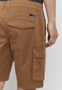 Brune cargo shorts laget av bomull. Funksjoner inkluderer sømde detaljer, flere lommer og en merkelapp festet til linningen.