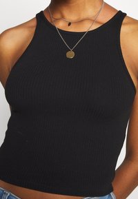 Débardeur noir à côtes avec une coupe ajustée, présentant un col haut et sans manches. Agrémenté de colliers en argent superposés.