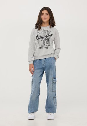 Felpa grigia con stampa 'City Girl New York', abbinata a pantaloni cargo azzurri chiari con tasche e vestibilità comoda. Sneakers bianche.