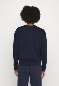 Námořnický modrý svetr s volným střihem, žebrovaným kulatým výstřihem a manžetami. Měkká tkanina a lem s vlnitým detailem. Nosen s odpovídajícími námořnickými kalhotami.