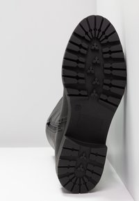 Bota negra con un upper de cuero texturizado, suela de goma resistente con patrones de dibujo profundos y una etiqueta de talla visible en la suela.