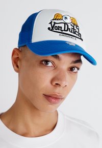 Sinine ja valge trucker kork, millel on silmapaistev "Von Dutch" logo tiibadega, võrgusilm seljaosa, kõver pidur ja reguleeritav nööpklamber.
