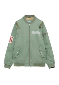 Veste bomber vert sauge avec fermeture éclair à l'avant, deux poches à rabat à bouton-pression, patch rayé rouge sur la manche gauche et texte blanc imprimé sur la poitrine.