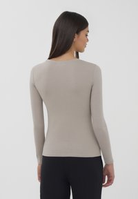Maglia a maniche lunghe in cotone beige chiaro, con scollatura rotonda e forma aderente. Texture liscia con cuciture minime.