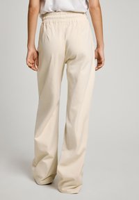Pantalones de pierna ancha beige hechos de algodón con una cinturilla elástica, que cuentan con bolsillos laterales y una textura suave.