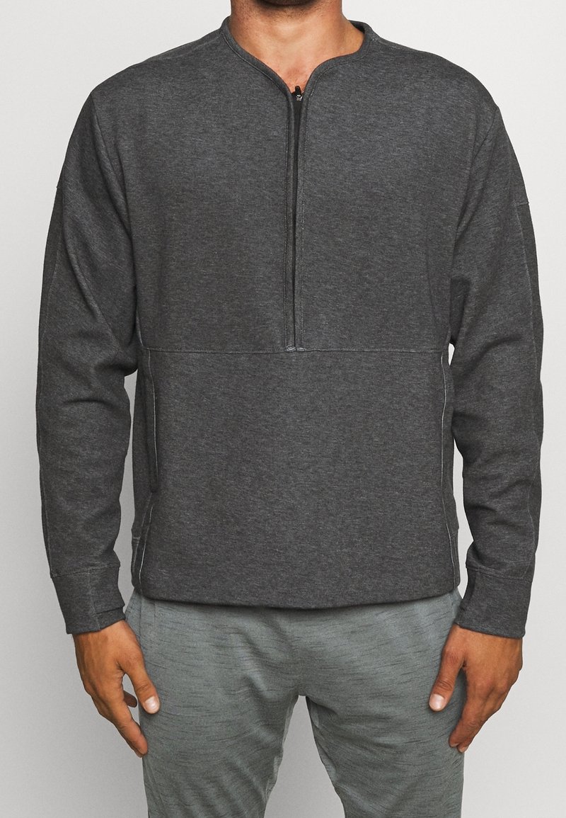 Pull-over gris foncé à manches longues avec un col à demi-fermeture éclair, doté d'un tissu lisse, de coutures contrastantes et de poches latérales.