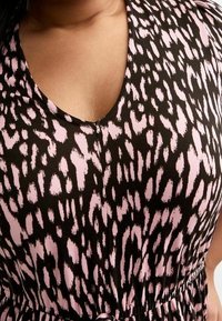Schwarzer Stoff mit rosa Leopardenmuster, ausgestattet mit einem V-Ausschnitt und elastischem Taillenzug. Glatte Textur mit Schulterakzenten.