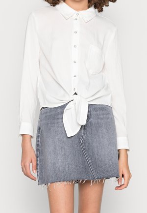 White button-up shirt with a knotted hem, paired with a gray denim skirt featuring frayed edges and a side seam.