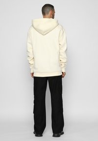Felpa con cappuccio crema a maniche lunghe e orlo a coste, abbinata a pantaloni cargo neri con più tasche e vestibilità rilassata.