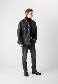 Black denim jacket with large pockets and buttons, paired with slim black jeans and black ankle boots. Smooth texture, minimalist design.