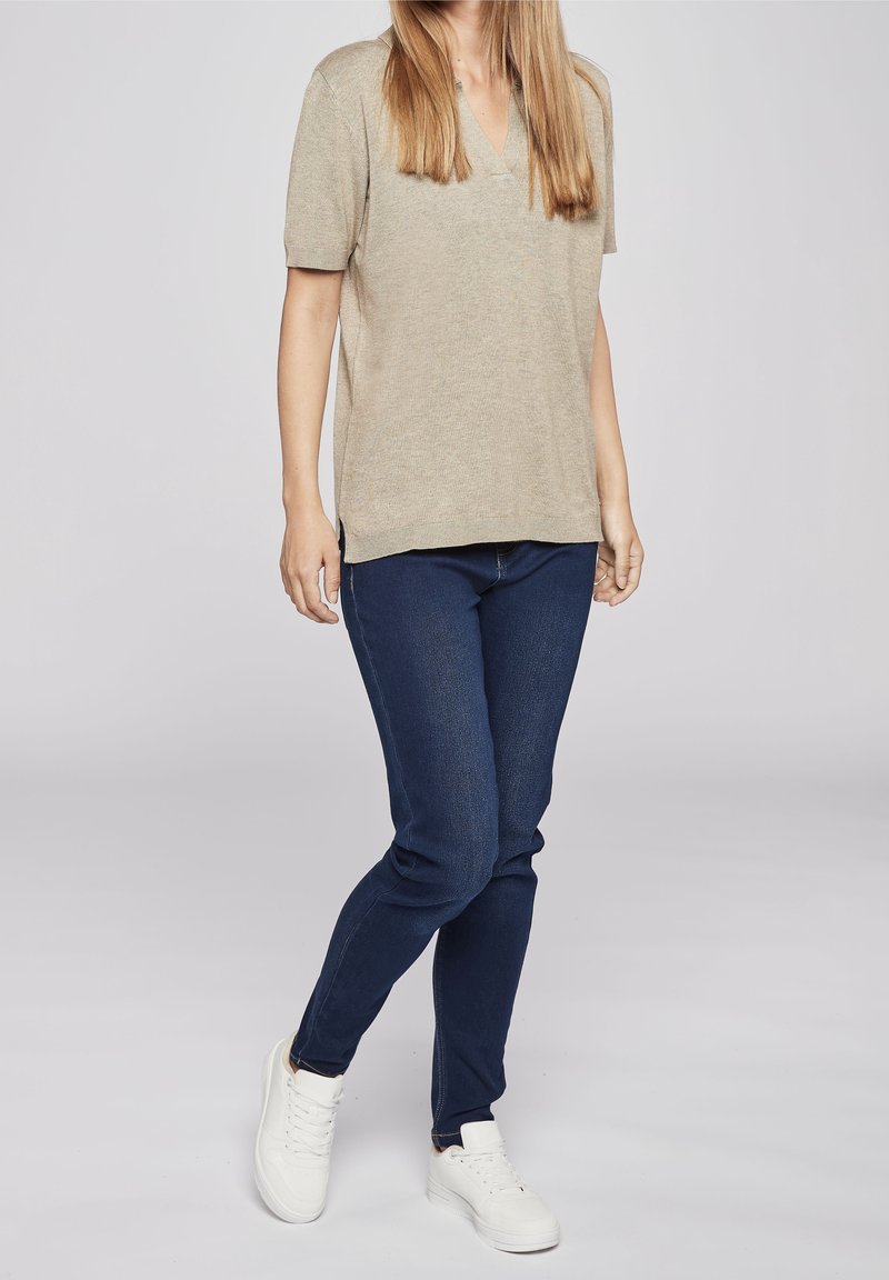 Beige stickad topp med korta ärmar och V-ringning, kombinerad med mörkblå stretchjeans och vita sneakers. Outfiten har en avslappnad passform.