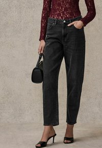 Jean en denim noir taille haute avec une coupe droite. Associé à un haut en dentelle bordeaux à manches longues et des chaussures à talons hauts noires sans lacets.
