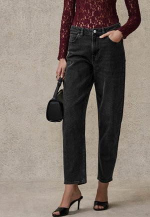 Jean en denim noir taille haute avec une coupe droite. Associé à un haut en dentelle bordeaux à manches longues et des chaussures à talons hauts noires sans lacets.