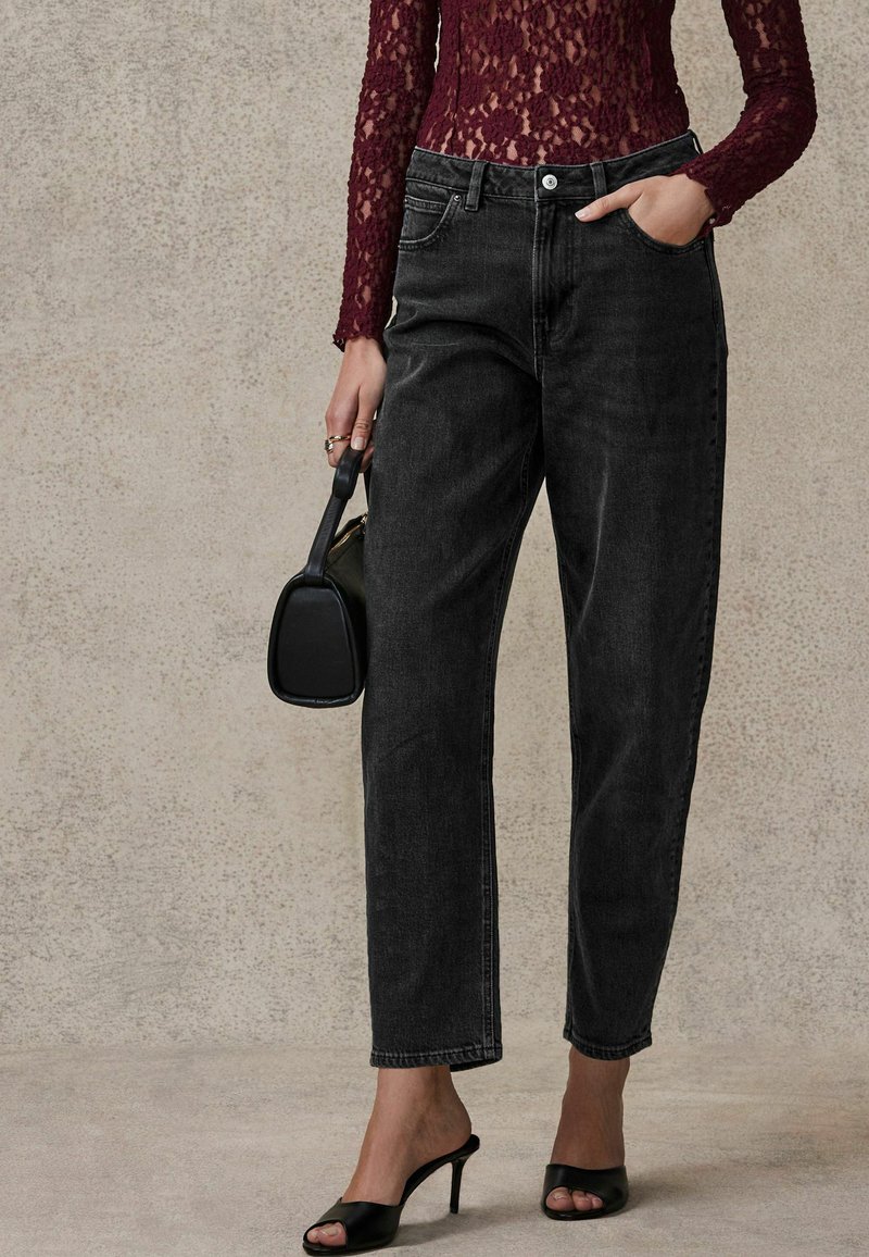 Jean en denim noir taille haute avec une coupe droite. Associé à un haut en dentelle bordeaux à manches longues et des chaussures à talons hauts noires sans lacets.