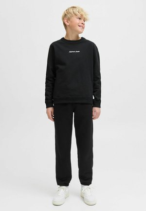 Svart bomullshoodie med ribbad ärmar och nederkant, med en vit broderad logotyp. Matchad med svarta sweatpants och vita sneakers.