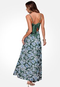 Vestido maxi con un patrón floral verde y flores azules, tirantes finos, espalda abierta con un detalle de lazo y tejido fluido.