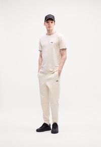 T-shirt crème avec des accents noirs, logo sur la poitrine ; pantalon de jogging crème assorti ; baskets noires ; design décontracté et sportif.