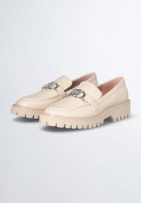 Mocassini in pelle beige con suola in gomma spessa, punta tonda e un accento in metallo argentato sulla cinghia anteriore. Texture liscia, design moderno.